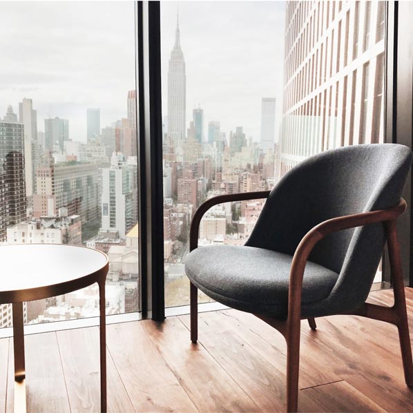 Scandinavian lounge chair beside a floor-to-ceiling window with Empire State Building views in an American Copper Building apartment, social content by The Charles Group