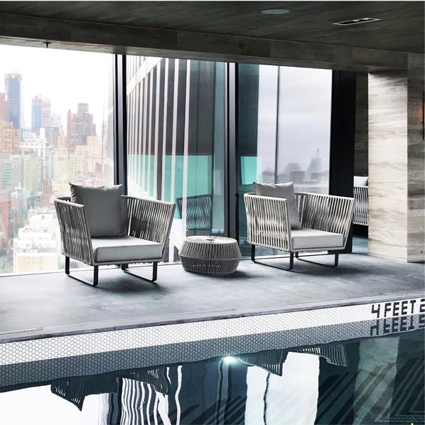 Woven lounge chairs beside an indoor lap pool with panoramic New York City skyline views at American Copper Buildings, social content by The Charles Group