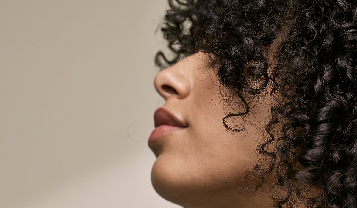 Close-up side profile of a woman with healthy, defined natural curls, hero image for Aveda global brand campaign by The Charles Group