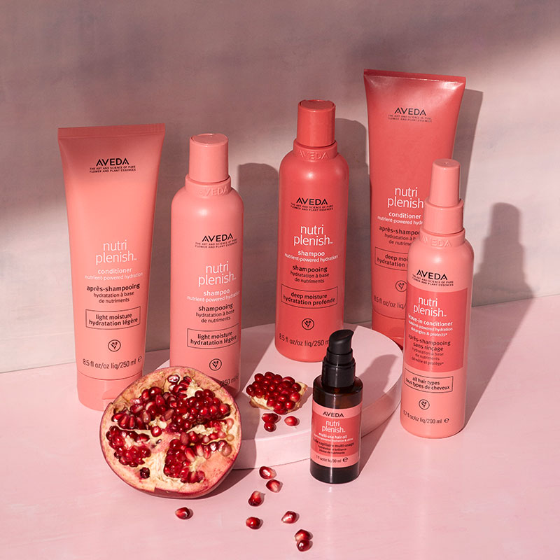 Full Aveda Nutriplenish haircare collection displayed with pomegranate fruit on a pink surface