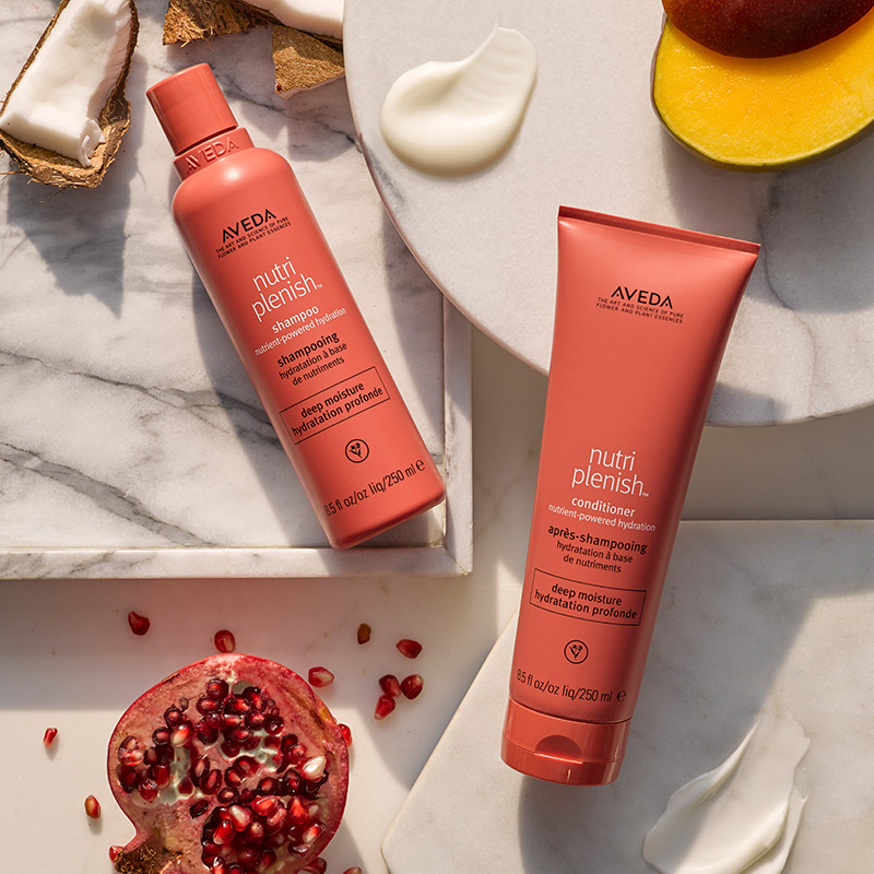 Aveda Nutriplenish deep moisture shampoo and conditioner duo arranged on tiered marble surfaces with pomegranate and mango