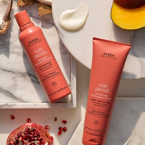 Aveda Nutriplenish deep moisture shampoo and conditioner duo on a marble surface with pomegranate and coconut ingredients, campaign content by The Charles Group