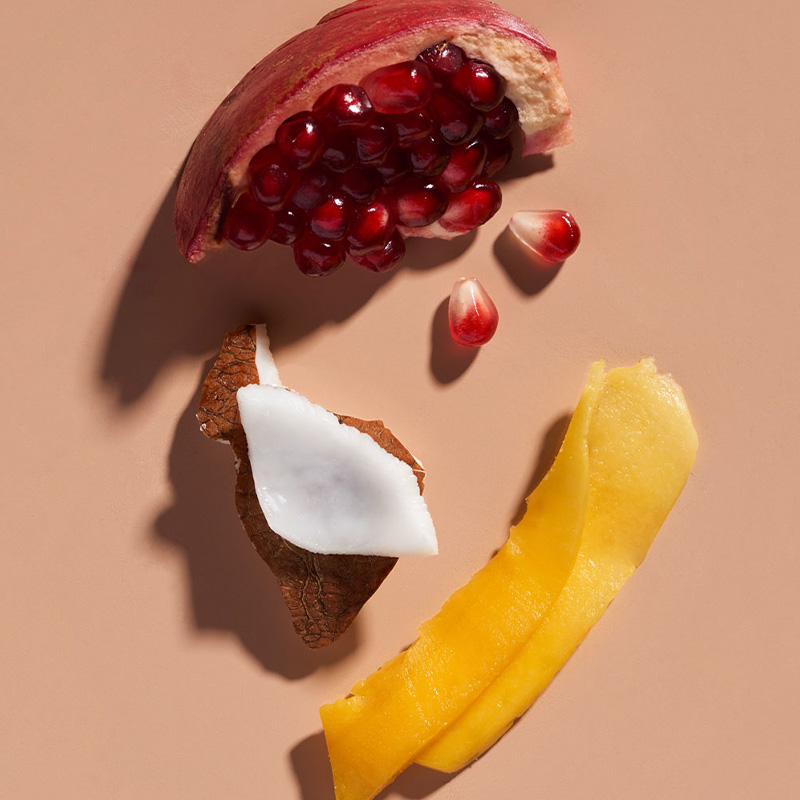 Flat lay of pomegranate, coconut, and mango — the natural superfood ingredients in Aveda Nutriplenish haircare