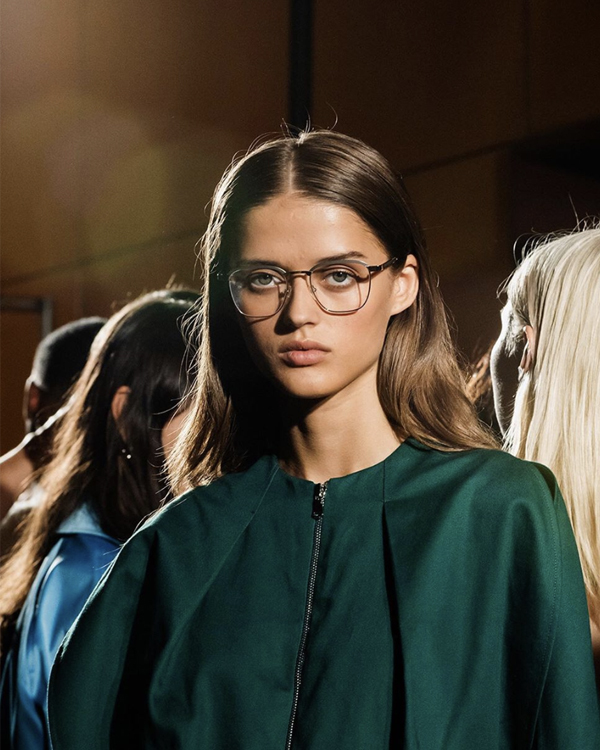 Model with sleek brunette hair and glasses backstage at an Aveda Runway fashion show, live event content by The Charles Group