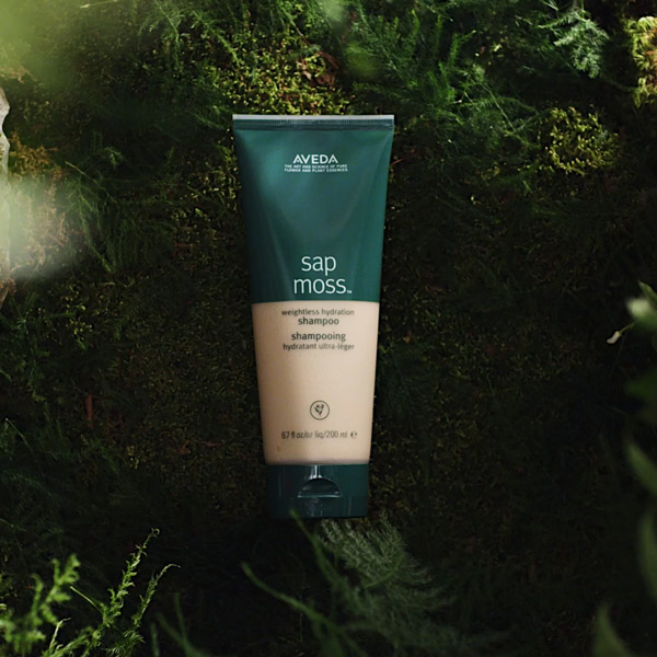 Aveda Sap Moss weightless hydration shampoo tube resting on a bed of green moss in a natural forest setting, social content by The Charles Group