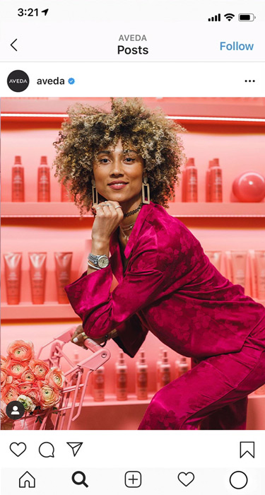 Model with curly hair in a magenta suit posing with a pink shopping cart at the Aveda Superfood Market event, Instagram content by The Charles Group