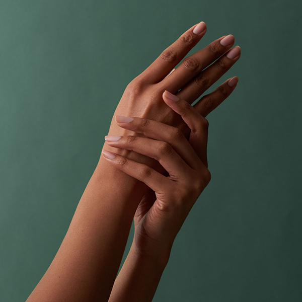 Raised hands with natural nails held together gracefully against a deep teal background, wellness campaign content for Aveda by The Charles Group