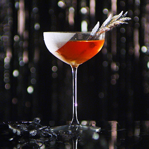 Elegant D'ussé cognac cocktail in a coupe glass garnished with a feathered sprig against a sparkling dark background, from D'ussé Holiday social campaign by The Charles Group