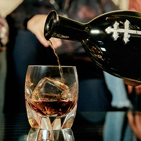 D'ussé XO cognac poured from the dark bottle into a crystal rocks glass with ice, social photography by The Charles Group
