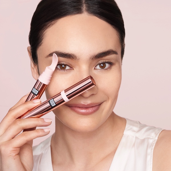 Model holding two Erno Laszlo eye gel cream applicator pens beside her face while smiling