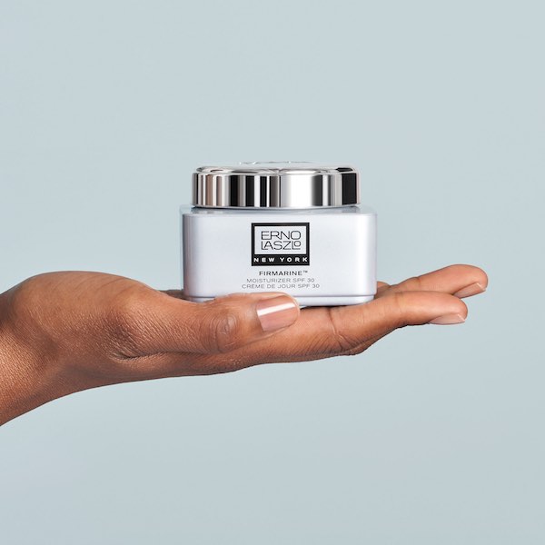Hand holding Erno Laszlo Firmarine SPF 30 moisturizer jar