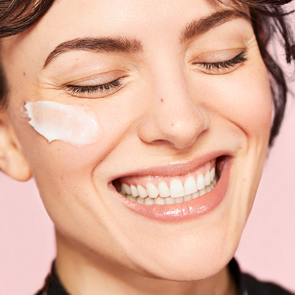 Model with cream swatch on cheek smiling in Erno Laszlo holiday campaign