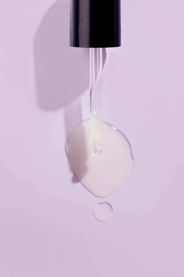 Close-up of a serum dropper dispensing a pool of Erno Laszlo AHA Resurfacing Sleep Serum on a lavender surface