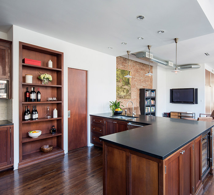 Open-plan loft kitchen with dark stone countertops, wood cabinetry, and exposed brick accent wall