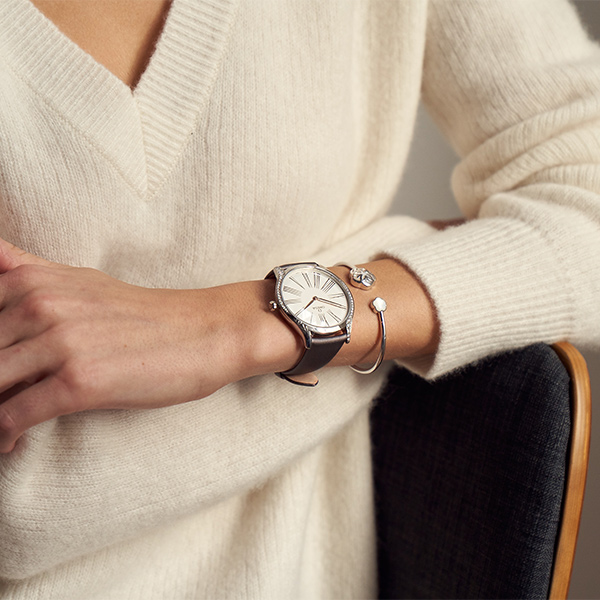 Woman in festive holiday outfit wearing Omega watch near a decorated Christmas tree, by The Charles Group