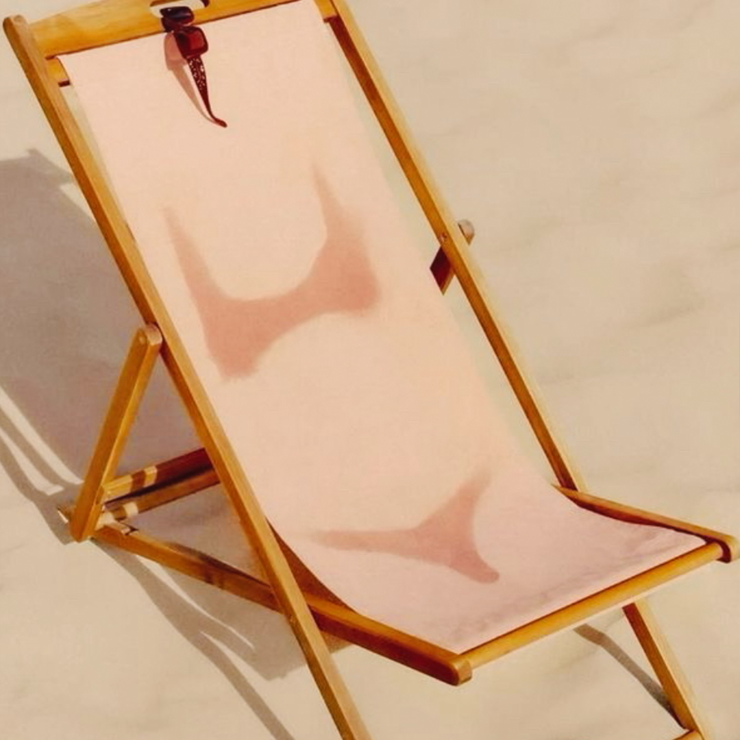 Vintage wooden deck chair casting a shadow on white sand, evoking classic coastal leisure at The Seagate Delray, from The Charles Group creative strategy