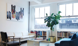 Bright loft-style creative workspace with sofa, fiddle leaf fig plant, bookshelves, and colorful wall art at The Charles Group NYC office