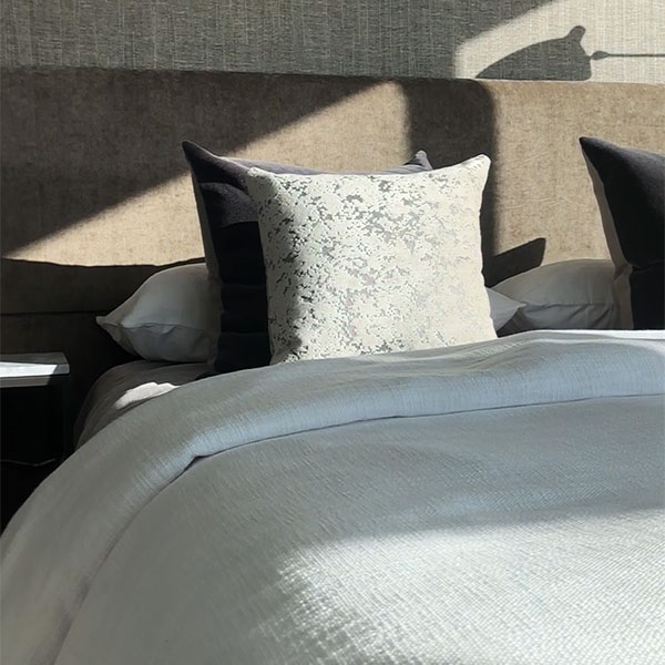 Close-up of a luxury bedroom with layered linen bedding and a textured decorative pillow in a Waterline Square apartment