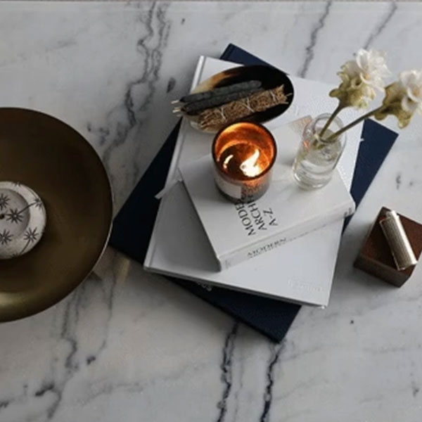Styled marble surface with stacked books, a lit amber candle, flowers, and a brass bowl in a Waterline Square luxury apartment