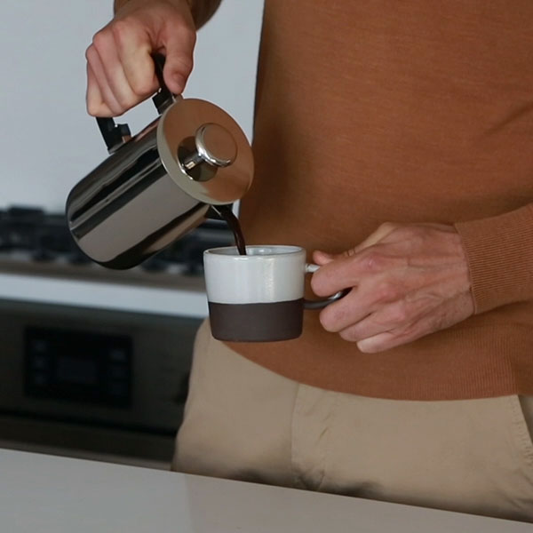 Resident pouring coffee from a French press in a modern luxury kitchen at Waterline Square NYC