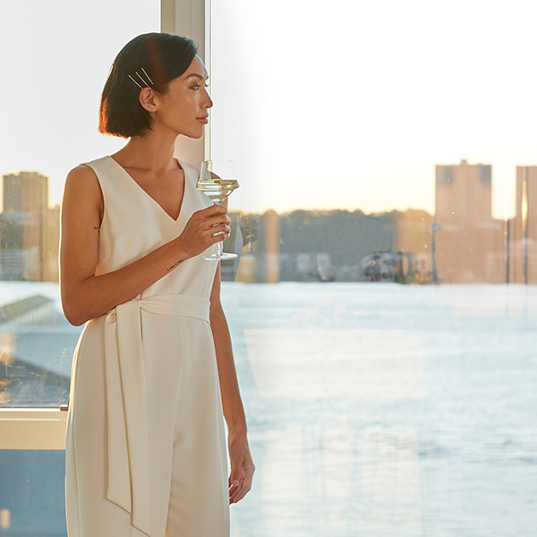 Woman in an elegant dress holding a martini glass while gazing at the Hudson River sunset from a Waterline Square luxury apartment