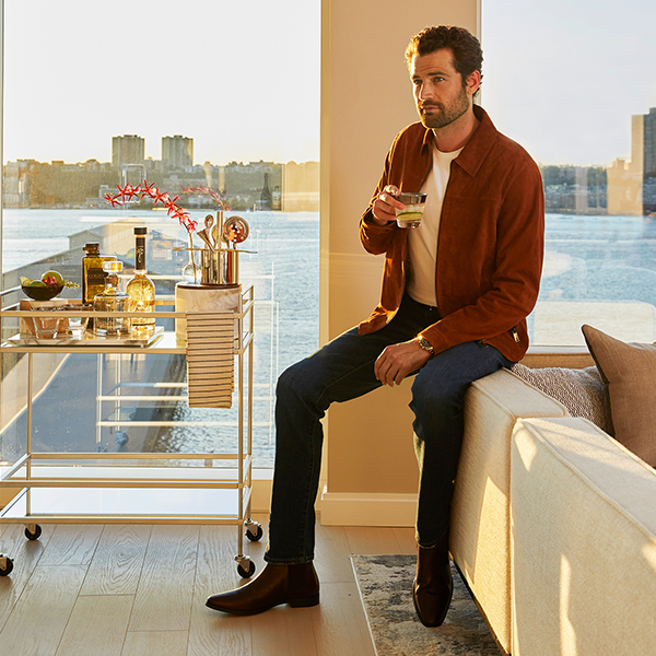 Man relaxing on a sofa with a cocktail in a Waterline Square luxury apartment with panoramic Hudson River views at golden hour