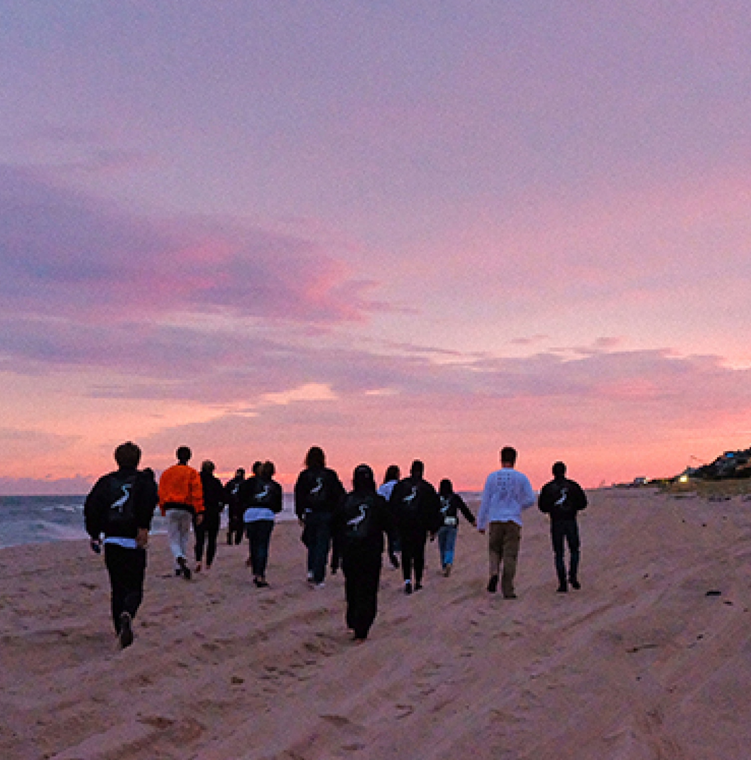 The Charles Group team walking together on the beach at sunset