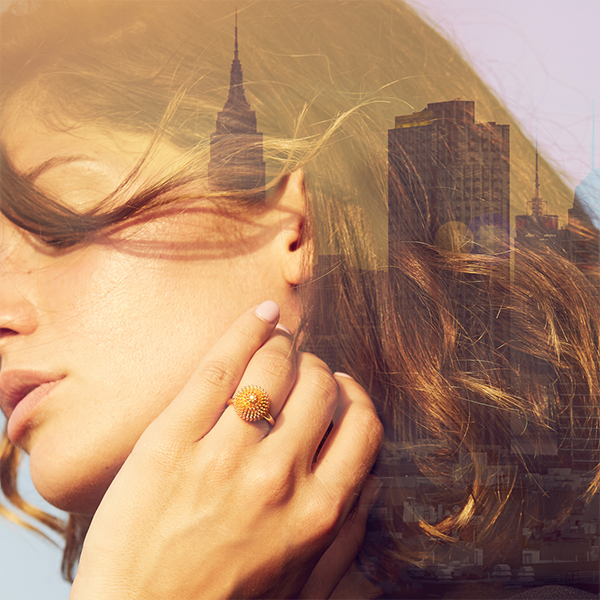 Double-exposure portrait of a woman wearing a Cartier Cactus de Cartier gold ring, overlaid with a city skyline