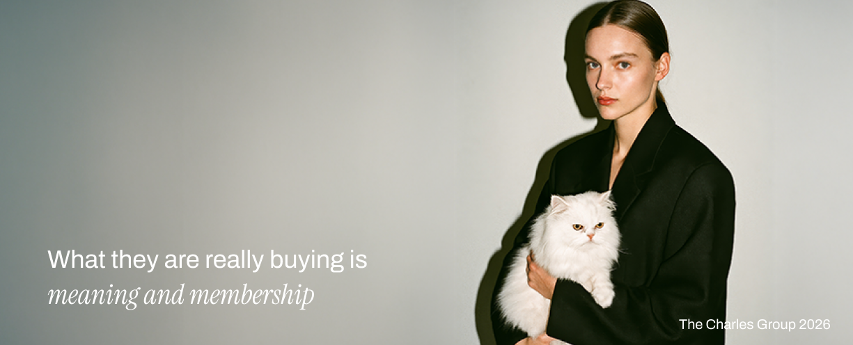 Fashion model in a black blazer holding a white Persian cat against a grey studio background, representing aspiration and status in luxury brand marketing